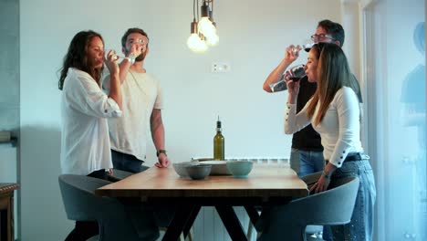 Smiling-friends-cheering-with-wineglasses-while-standing-near-table